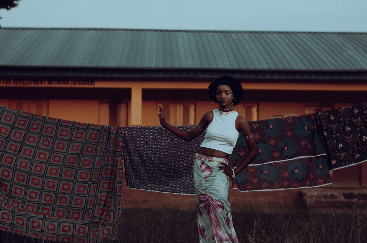 A stylish young woman standing near vibrant fabrics outdoors in Lagos, Nigeria.