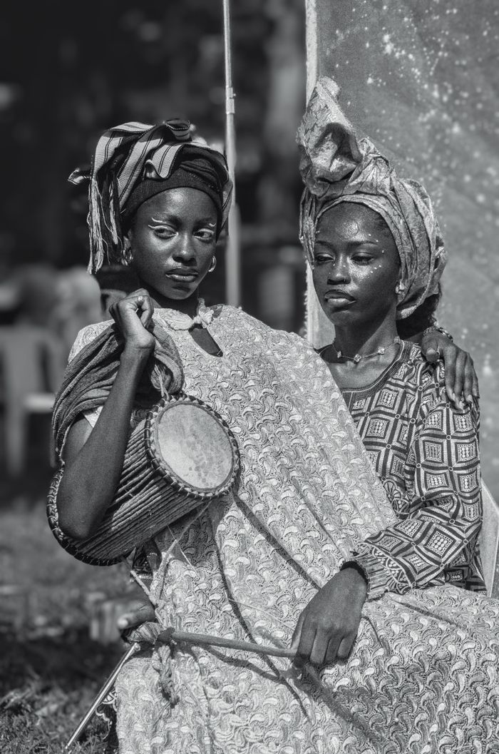 Two Nigerian women in traditional attire holding a drum, depicting cultural heritage in Nigeria.