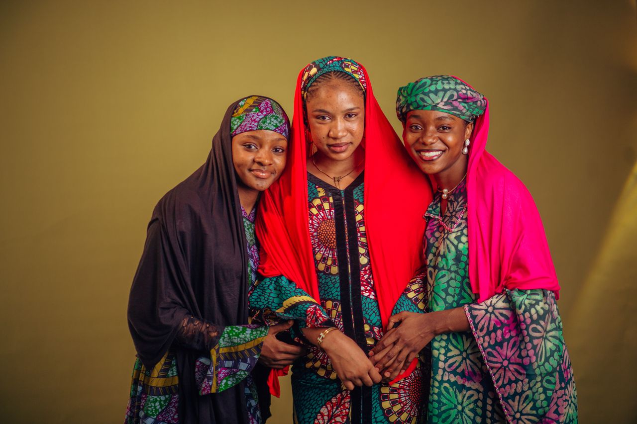 Three Nigerian women in vibrant Hausa attire, showcasing cultural fashion.